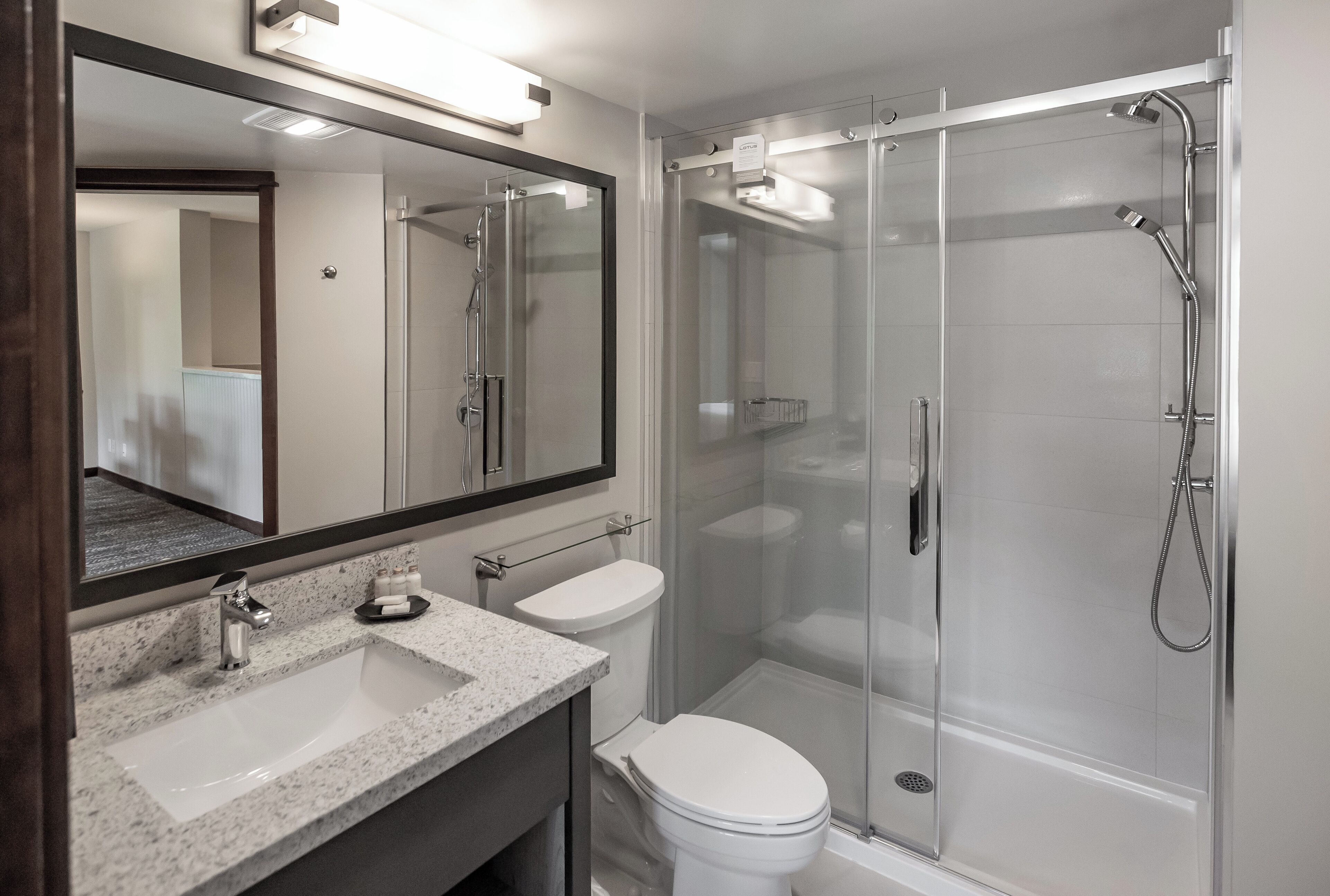 A modern bathroom with a large mirror, a sink, a toilet, and a glass-enclosed shower area.