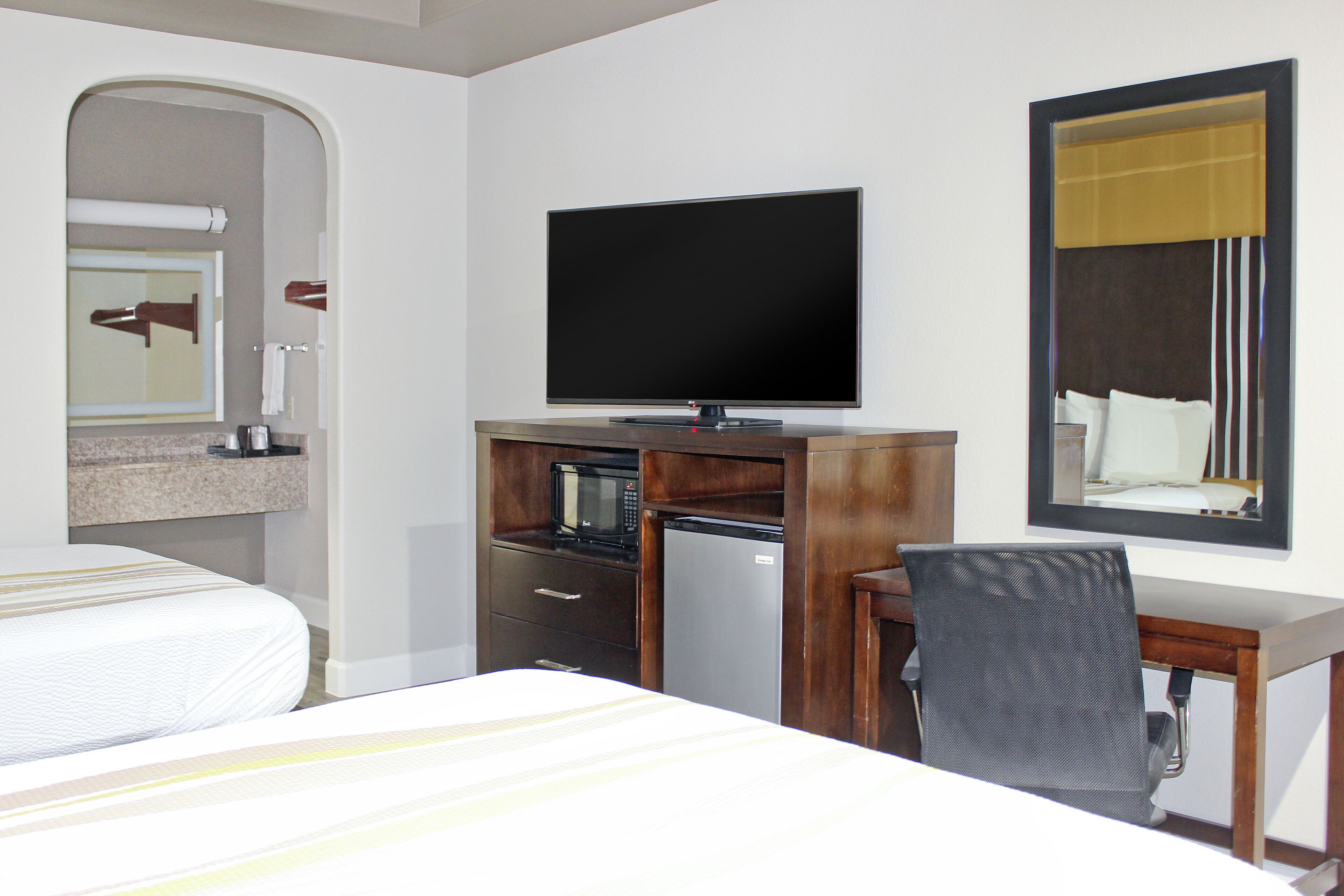Ein Hotelzimmer mit Bett, Schreibtisch mit Stuhl, Fernseher, Mikrowelle und Kühlschrank.