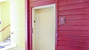 A building entrance with a red exterior, a beige elevator door, and a stairway with a handrail. - Palacio Royale Inn Houston NW Beltway 8 (Houston)
