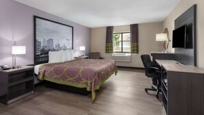 A hotel room with a bed, desk, chair, TV, and cityscape artwork. - Super 8 by Wyndham Copley Akron (Akron)