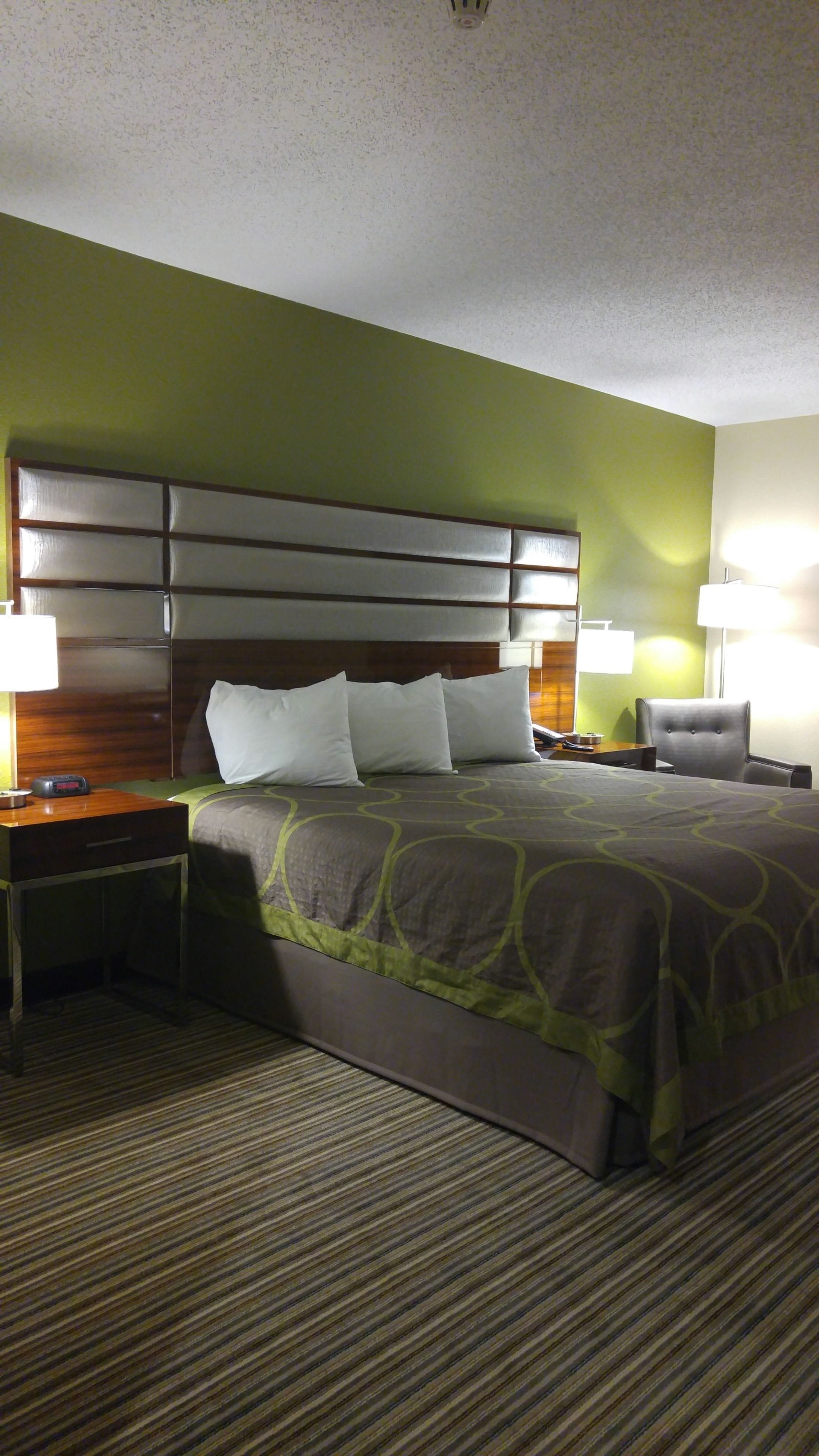 A hotel room with a large bed, two bedside tables, a chair, and a headboard.