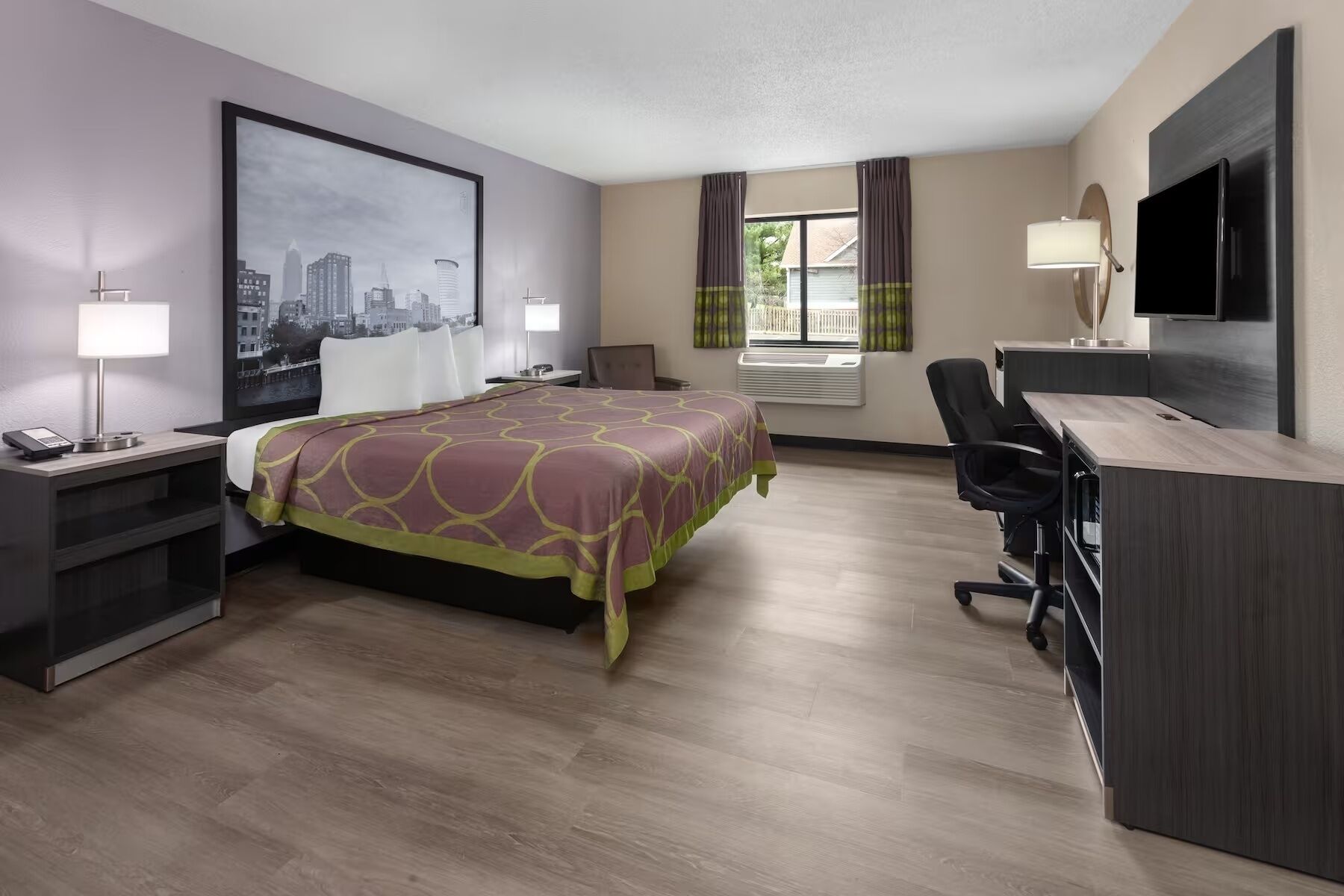 Een hotelkamer met een bed, bureau, stoel, televisie en uitzicht op de stad.
