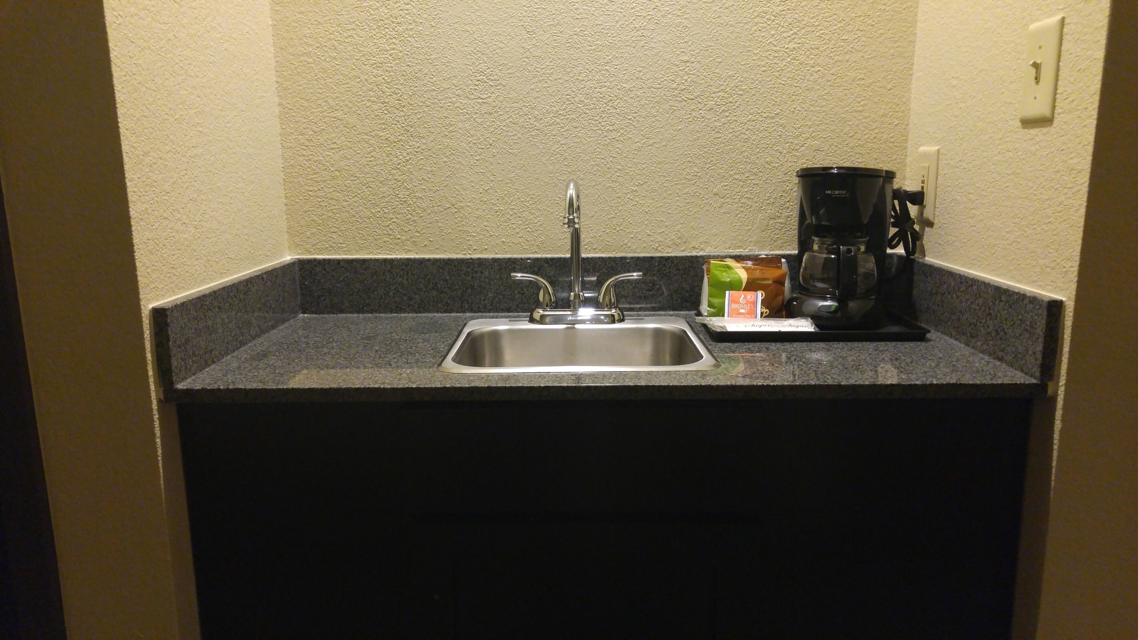A small kitchen with a sink, a coffee maker, and a packet of sugar.
