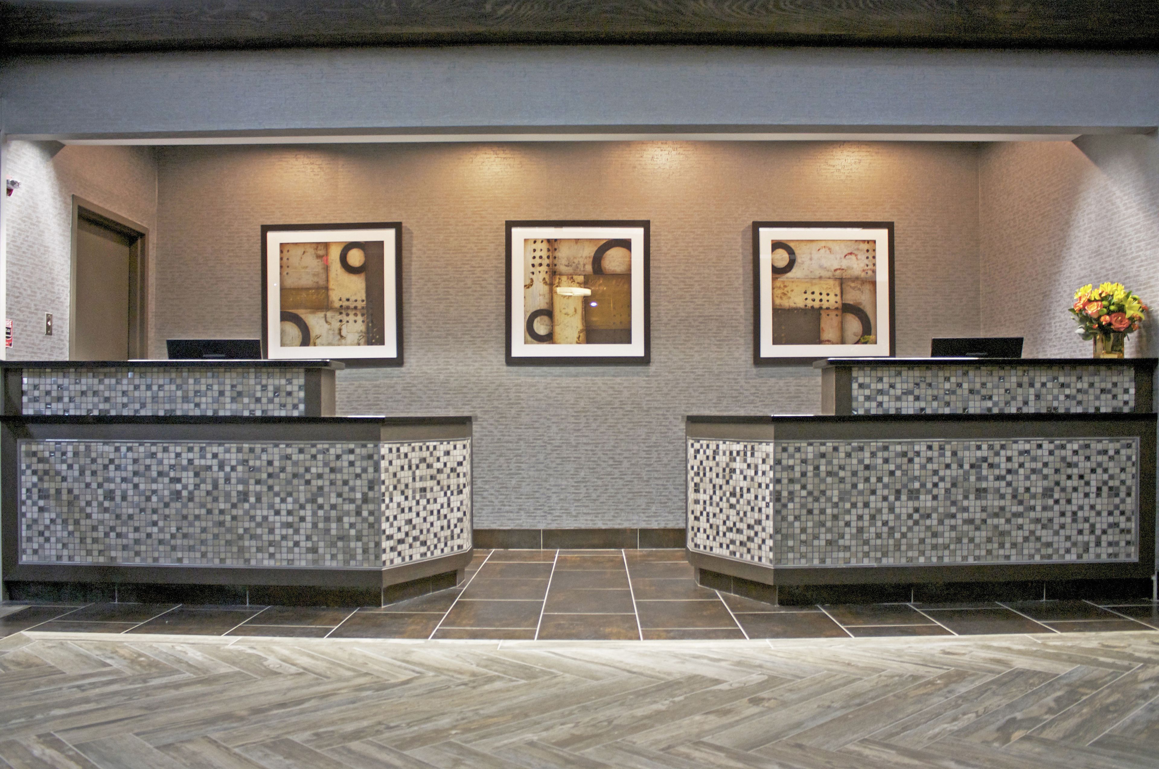 A reception area with a herringbone patterned floor, a tiled wall, and three framed abstract artworks above the reception desk.
