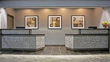 Un área de recepción con piso de patrón espiga, pared azulejada y tres obras de arte abstracto enmarcadas sobre el mostrador de recepción.