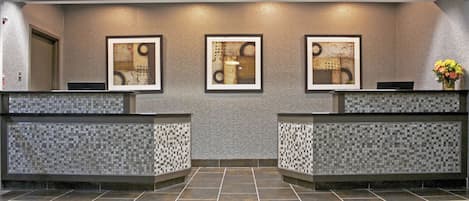 A reception area with a herringbone patterned floor, a tiled wall, and three framed abstract artworks above the reception desk.