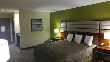 A hotel room with a large bed, a bedside table with a lamp, a nightstand with a phone, and a framed picture on the wall.