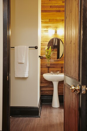 A bathroom with a white sink, a wooden wall, a mirror, and a towel hanging on a rack.