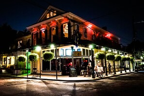 A historic building with a cafe on the ground floor, outdoor seating, and hanging plants. - Royal Street Inn and R Bar (New Orleans)