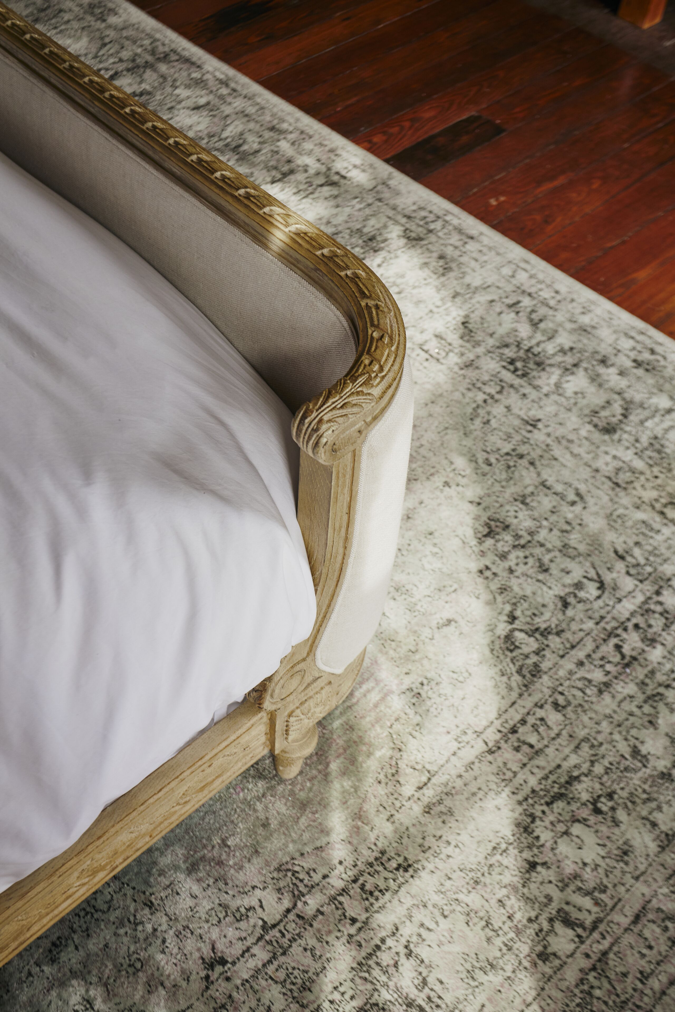 A bed with a wooden frame and a white mattress, positioned on a patterned rug.