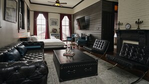 Ein geräumiges Wohnzimmer mit einer großen schwarzen Ledersofa, einem passenden Sessel und einem Couchtisch. Darüber befindet sich ein Kamin mit einer Uhr und Kerzenhaltern.