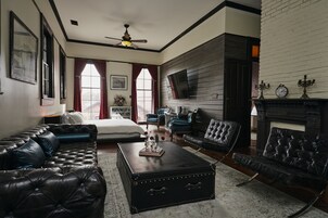 Amplia sala de estar con un sofá grande de cuero negro, un sillón a juego y una mesa de centro. Cuenta con una chimenea con un reloj y candelabros arriba.