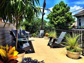 An outdoor patio area with multiple lounge chairs and tables, surrounded by potted plants and trees.
