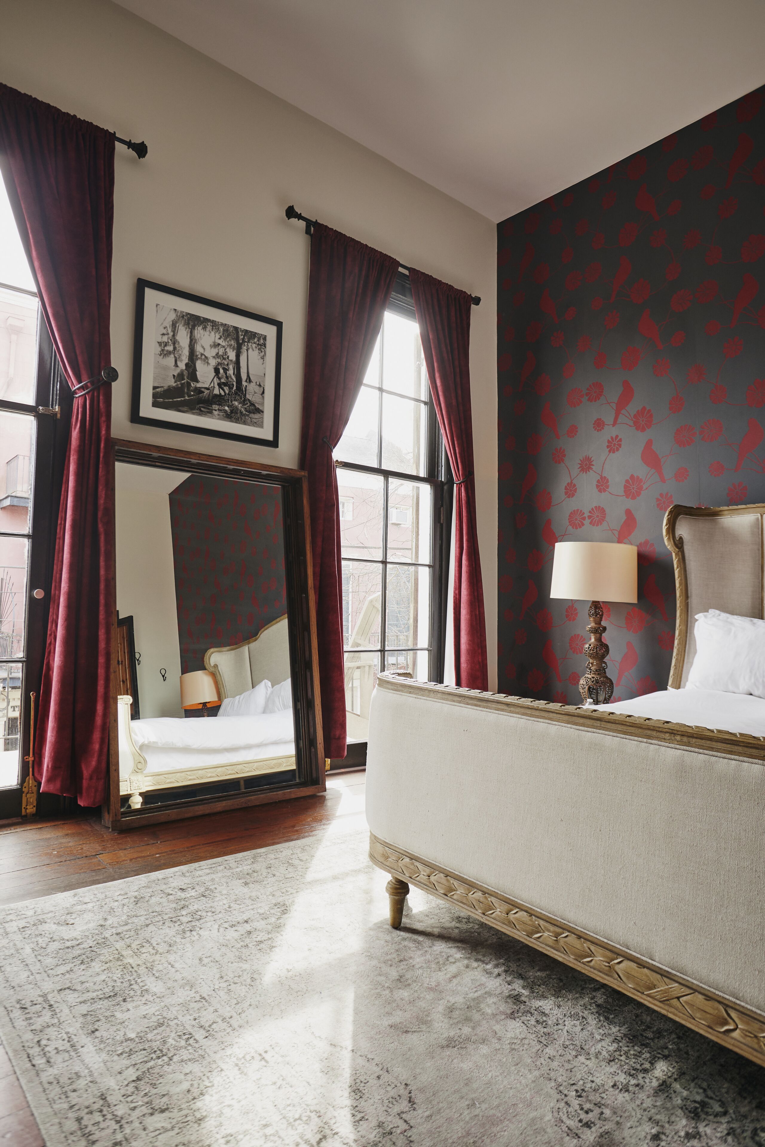 A bedroom with a bed, a nightstand, a mirror, and a window with curtains.