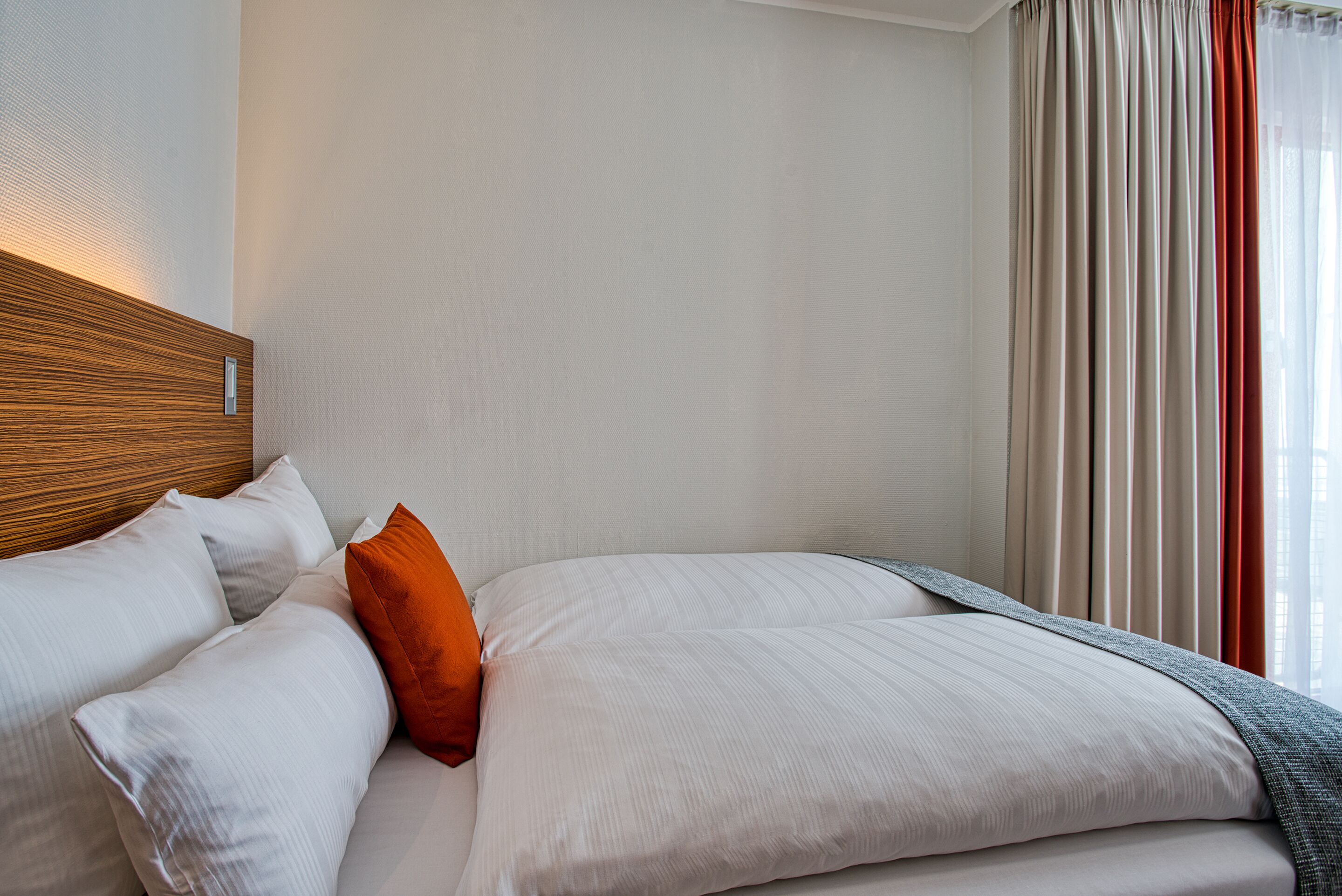 A neatly made bed with white and orange pillows, a wooden headboard, and a grey blanket.