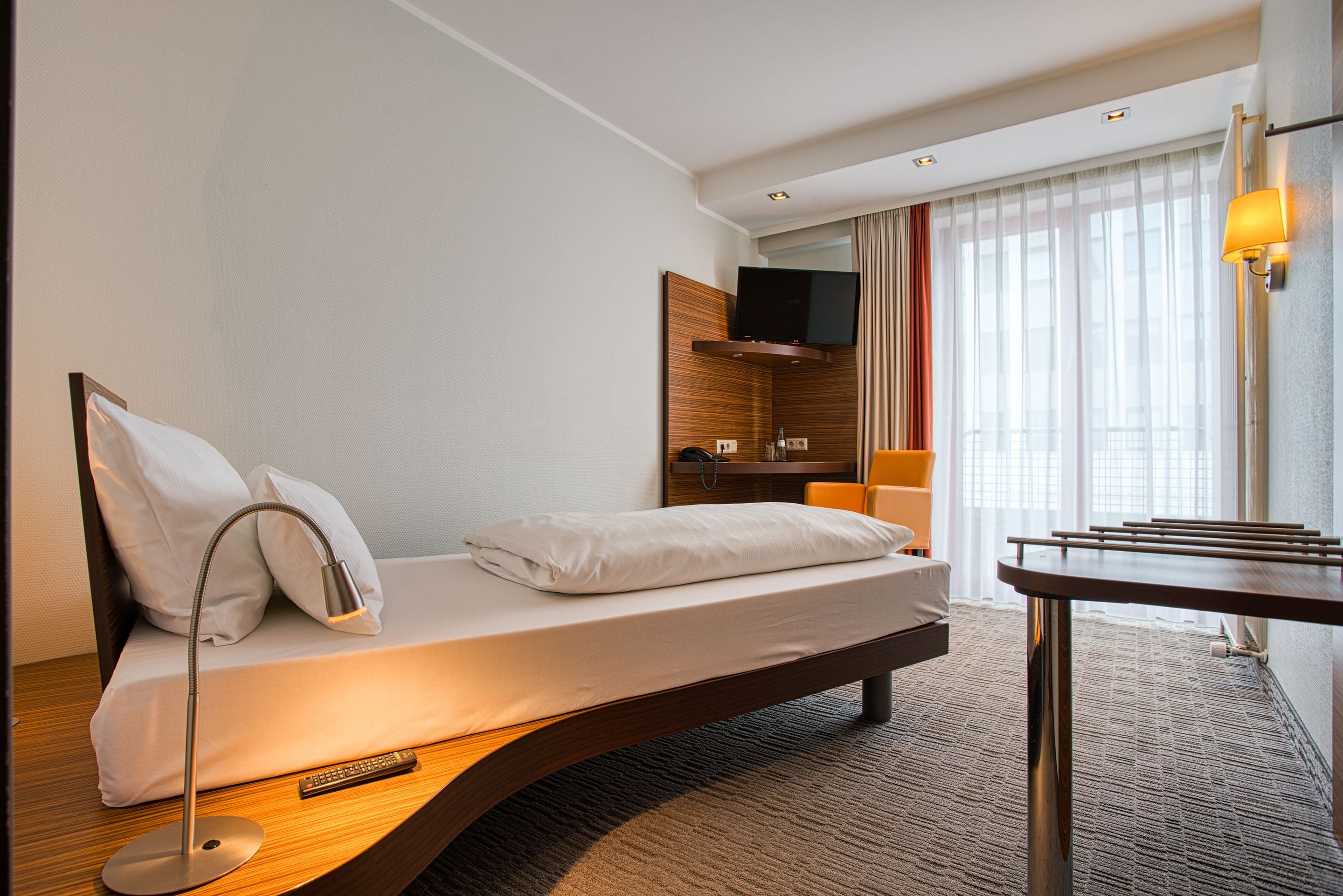 Camera d'albergo moderna con un letto singolo, una scrivania, una sedia, una TV e una finestra con tende.