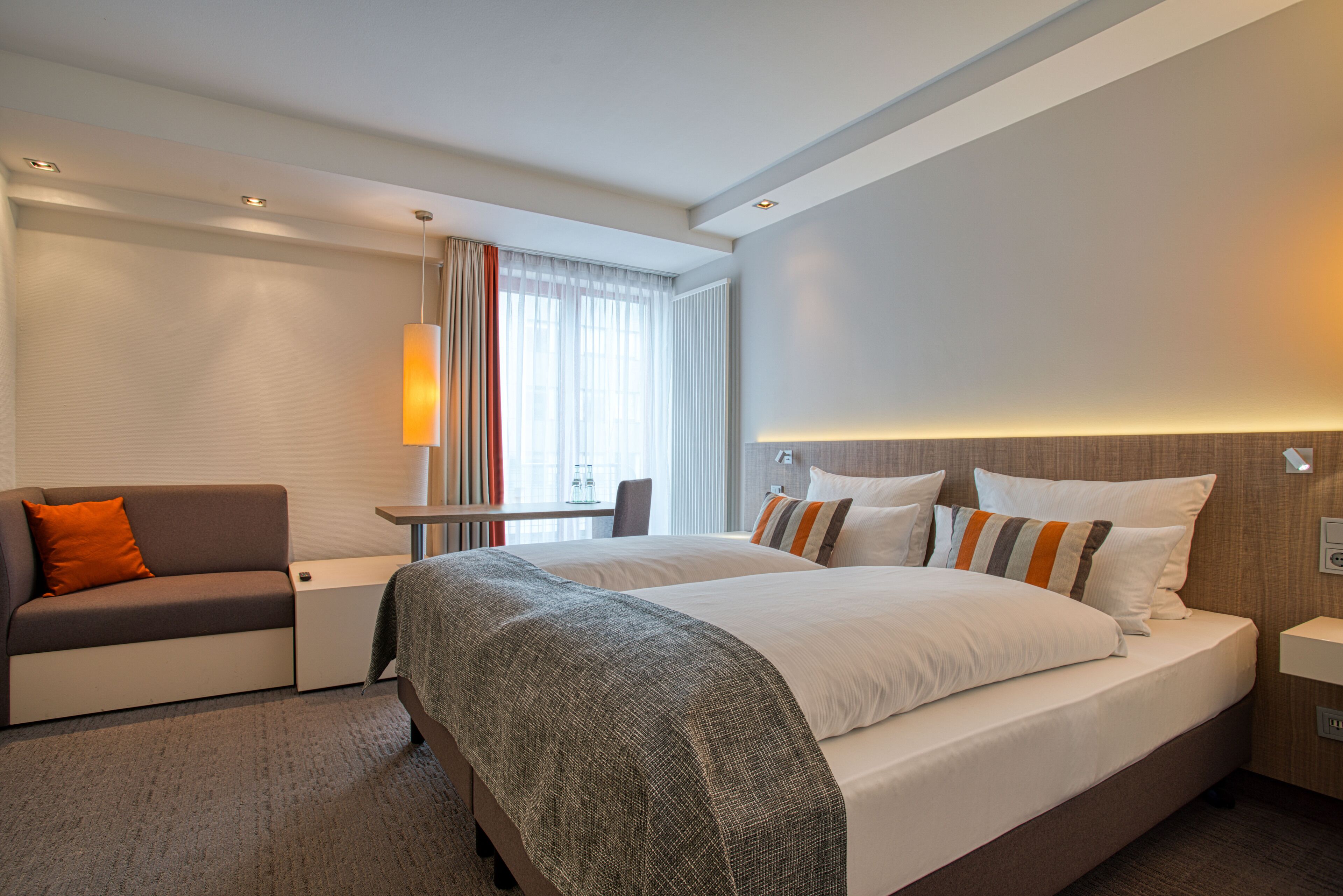 Une chambre d’hôtel avec un grand lit, un canapé, un bureau et une fenêtre avec des rideaux.