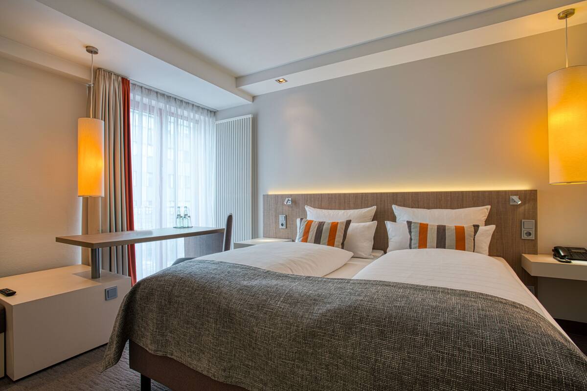 Una habitación de hotel con una cama grande, mesitas de noche, un escritorio y una ventana con cortinas.