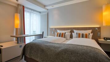 A hotel room with a large bed, bedside tables, a desk, and a window with curtains.