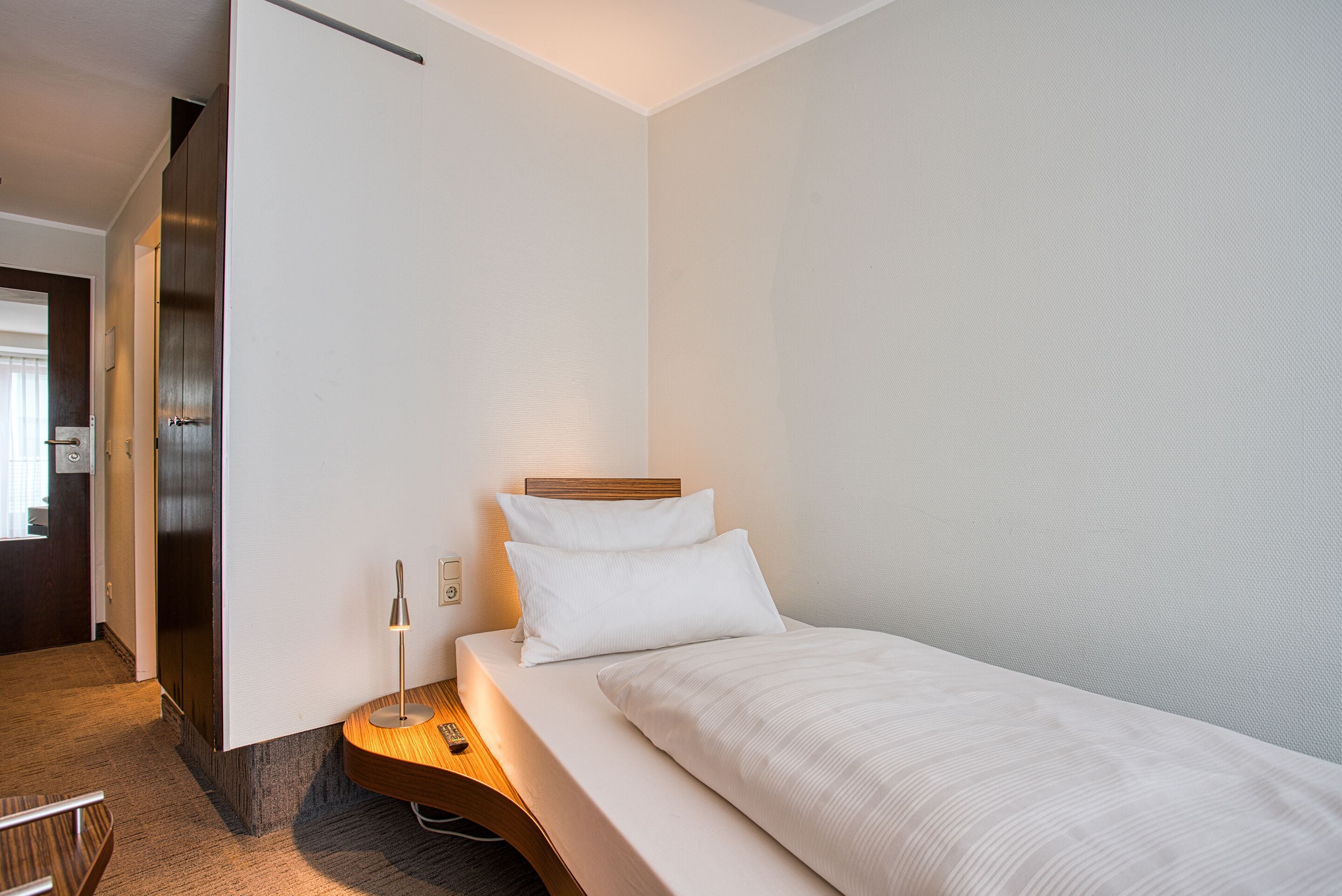 A modern hotel room with a bed, a desk, and a lamp.