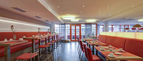 A modern restaurant with red booths and high tables, featuring a central walkway and large windows.