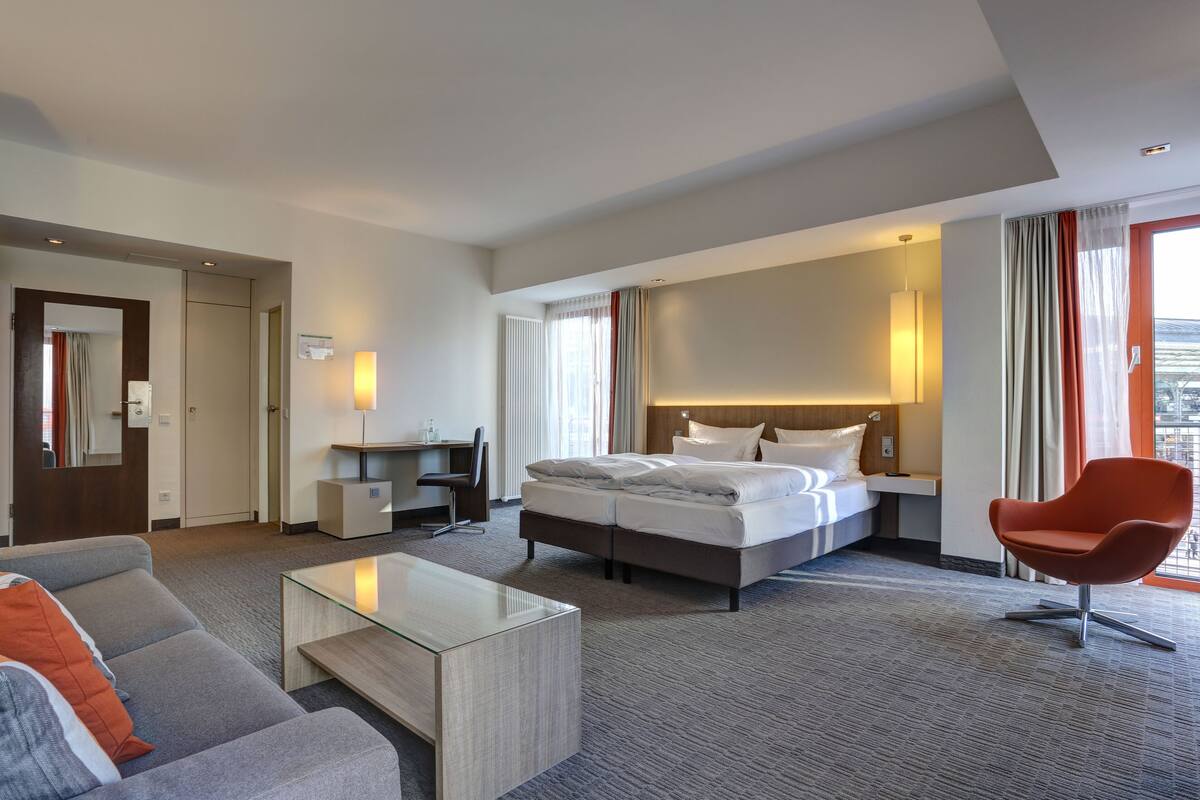 Una habitación de hotel moderna con cama, escritorio, silla y sofá.
