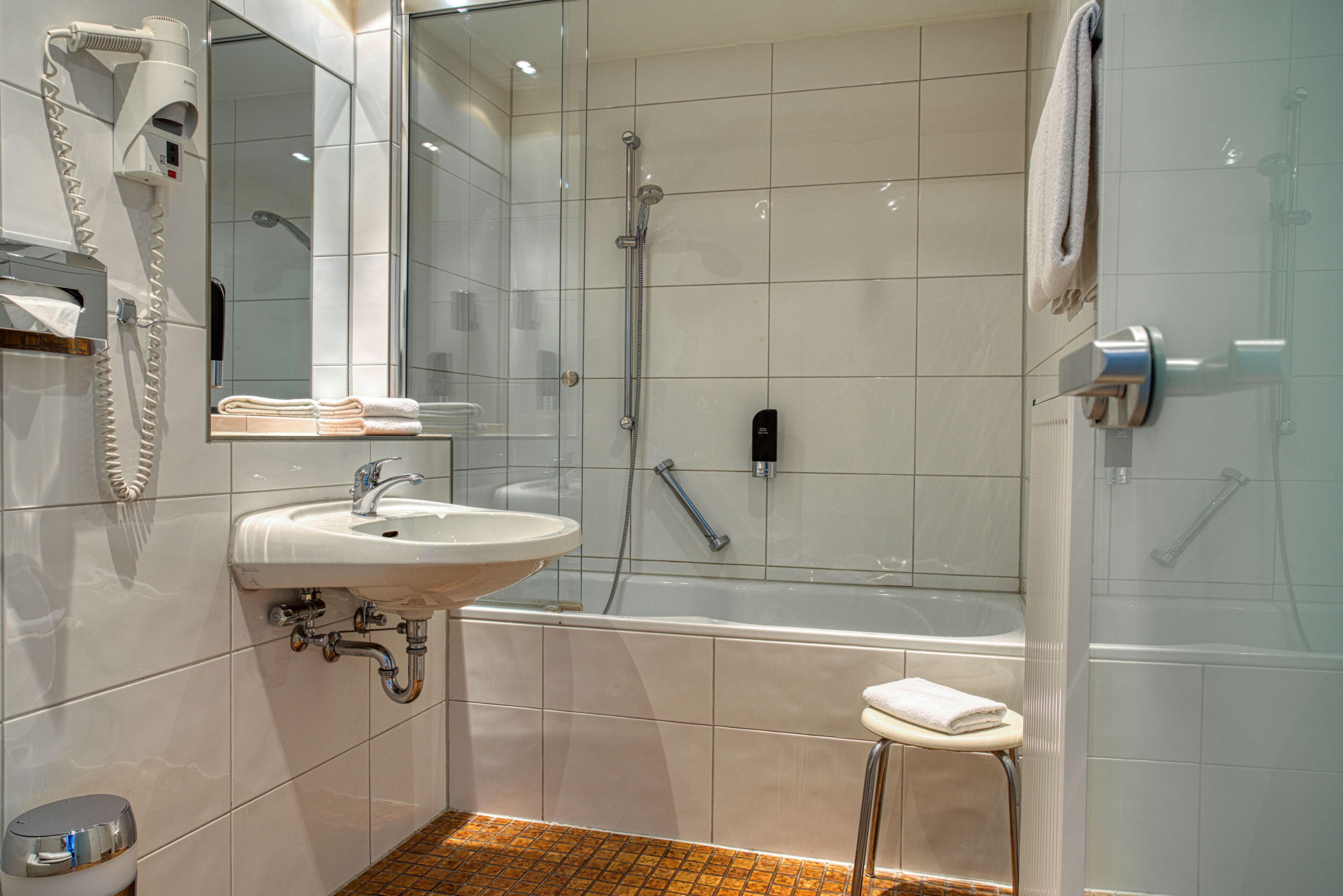A modern bathroom with a sink, mirror, towel rack, and shower.