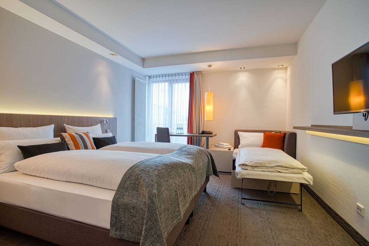 Habitación de hotel con dos camas, un escritorio, una silla, un televisor y una ventana con cortinas.