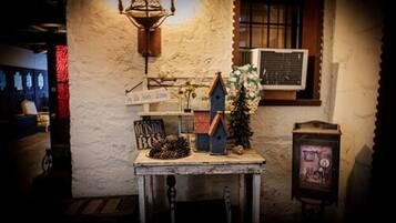 Un interior rústico con una pared de piedra, una mesa de madera con un letrero que dice "OUTSIDE BO", un comedero para pájaros y un pequeño árbol de Navidad.