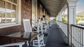 Un espace extérieur abrité, avec des chaises et des tables blanches, un mur de briques et une vue sur un paysage vallonné.