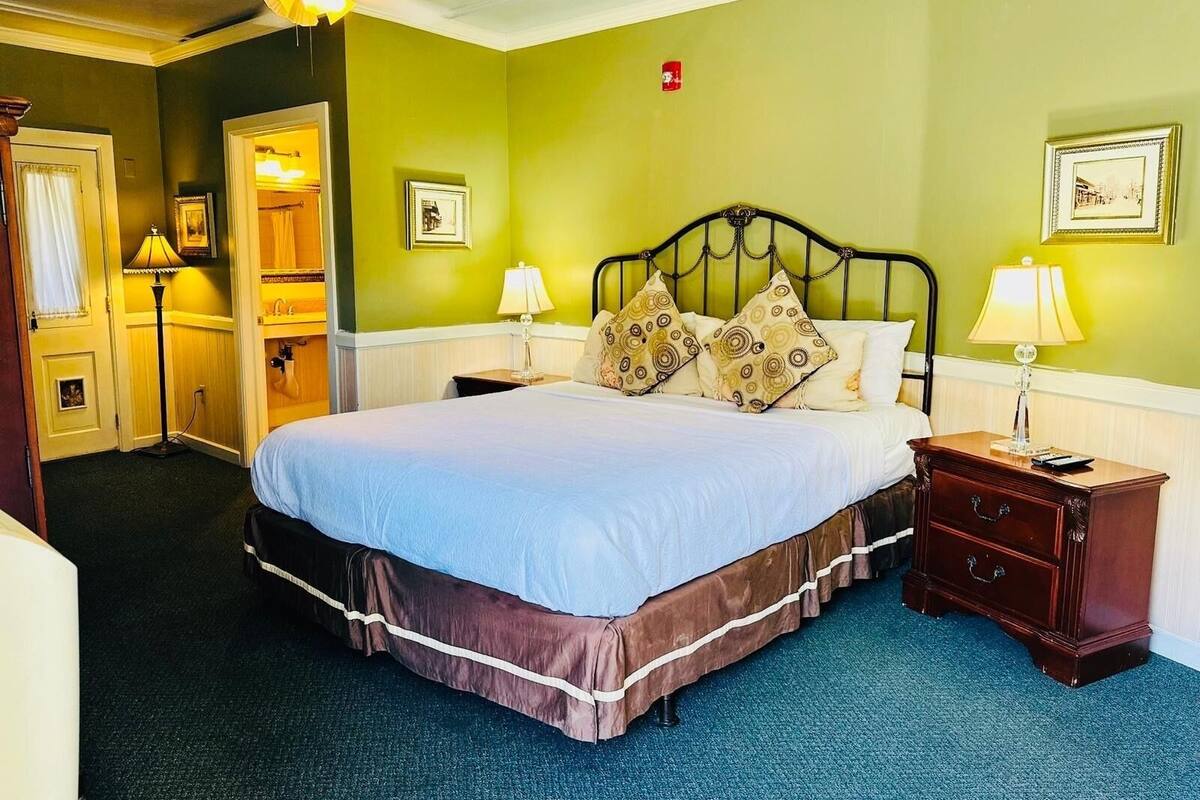 A hotel room with a large bed, two bedside tables with lamps, a ceiling fan, and a door leading to a bathroom.