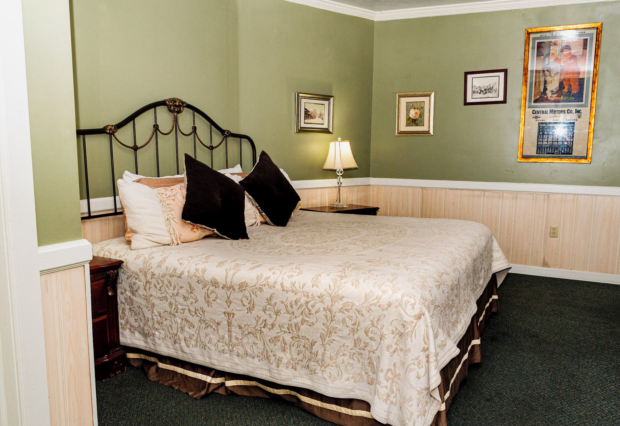 A neatly made bed with a floral bedspread, a nightstand with a lamp, and framed pictures on the wall.