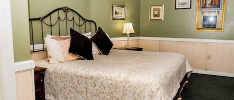 A neatly made bed with a floral bedspread, a nightstand with a lamp, and framed pictures on the wall.