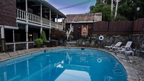 Une piscine avec une terrasse en bois, des chaises longues et un mur en pierre.