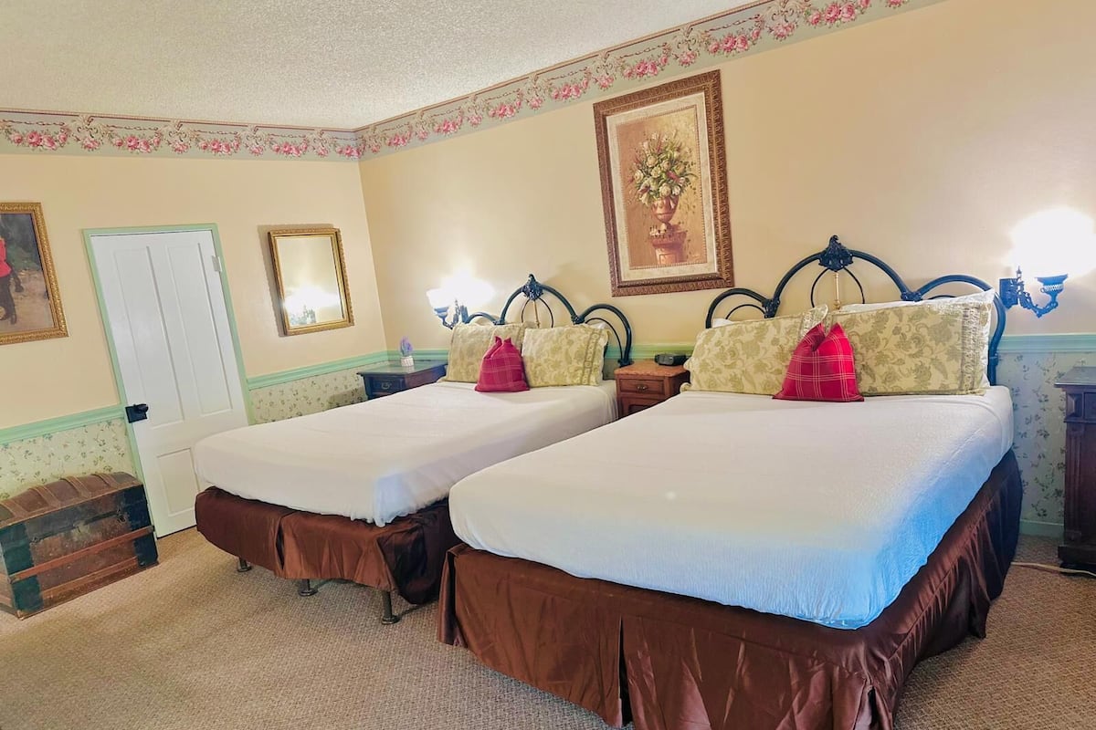 A hotel room with two beds, a door, a mirror, and a floral wall decoration.