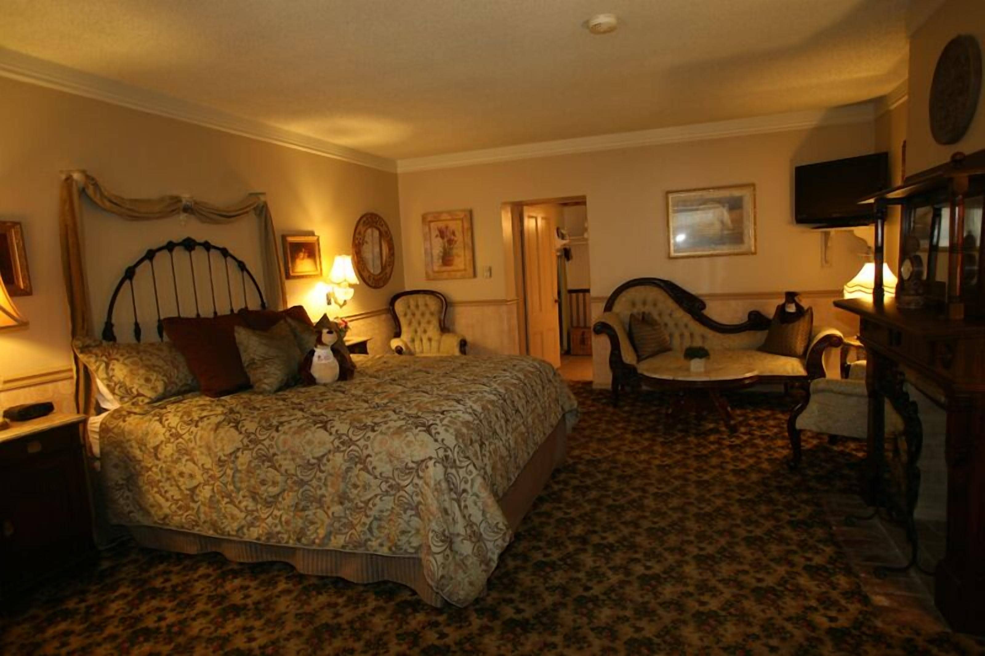 A bedroom with a large bed, two armchairs, a small table, and a television.