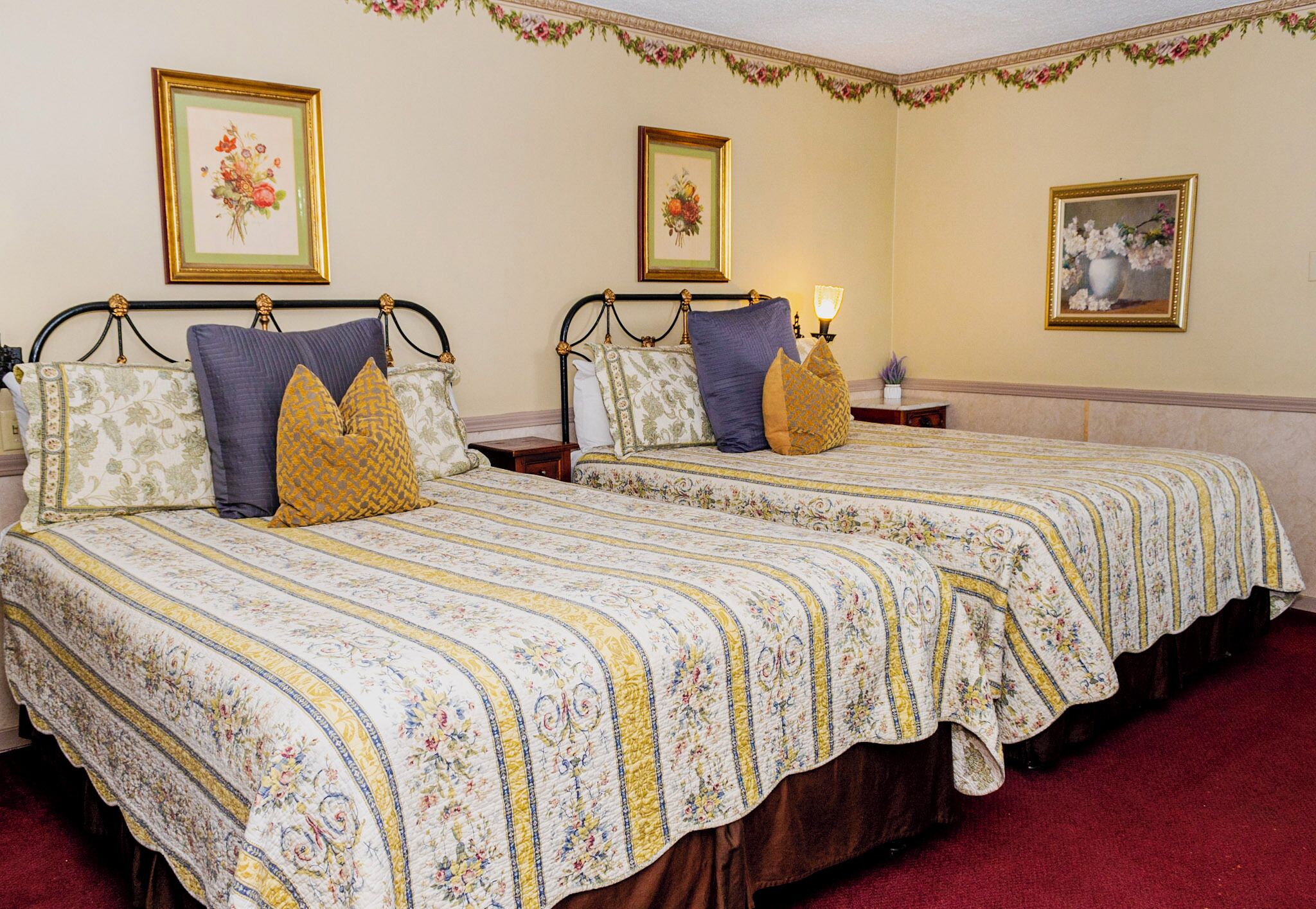 A hotel room with two beds, floral-patterned bedding, and framed floral artwork on the walls.