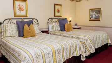 A hotel room with two beds, floral-patterned bedding, and framed floral artwork on the walls.