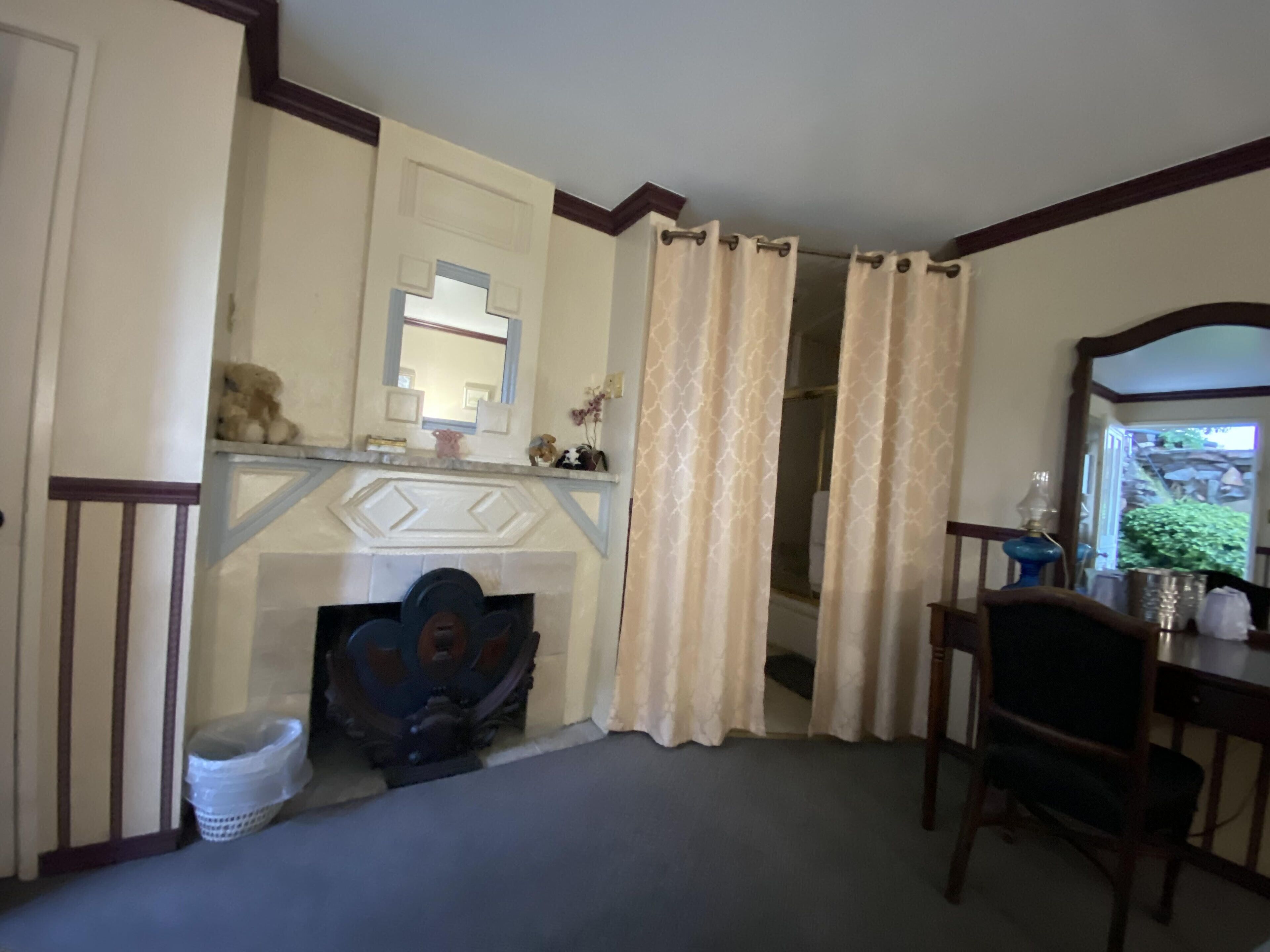 A room with a fireplace, a mirror, a chair, and a desk.