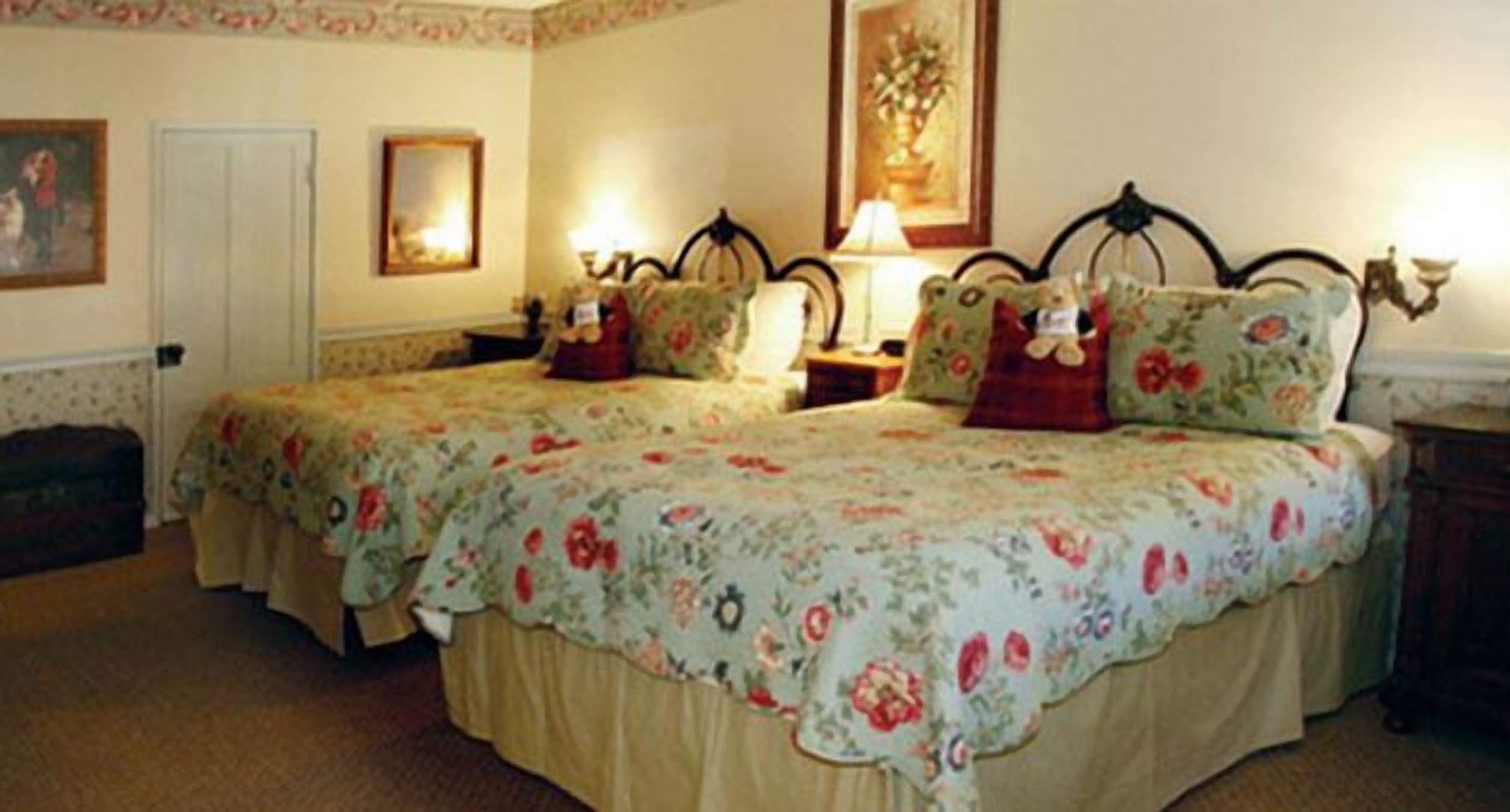 A room with two beds, floral bedspreads, wall-mounted lamps, and framed artwork.
