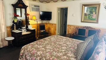 A bedroom with a floral bedspread, a dresser with a mirror, a television, and a painting on the wall.