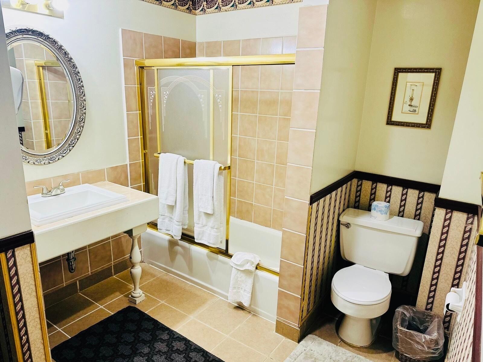 A bathroom with a white sink, a gold-framed mirror, a bathtub with a gold shower curtain, and a toilet.