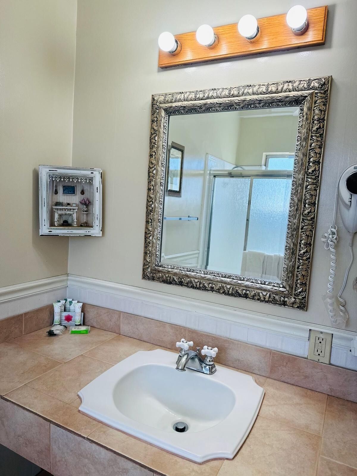Casa de banho com um espelho grande e trabalhado, uma sanita e um secador de cabelo fixado na parede.