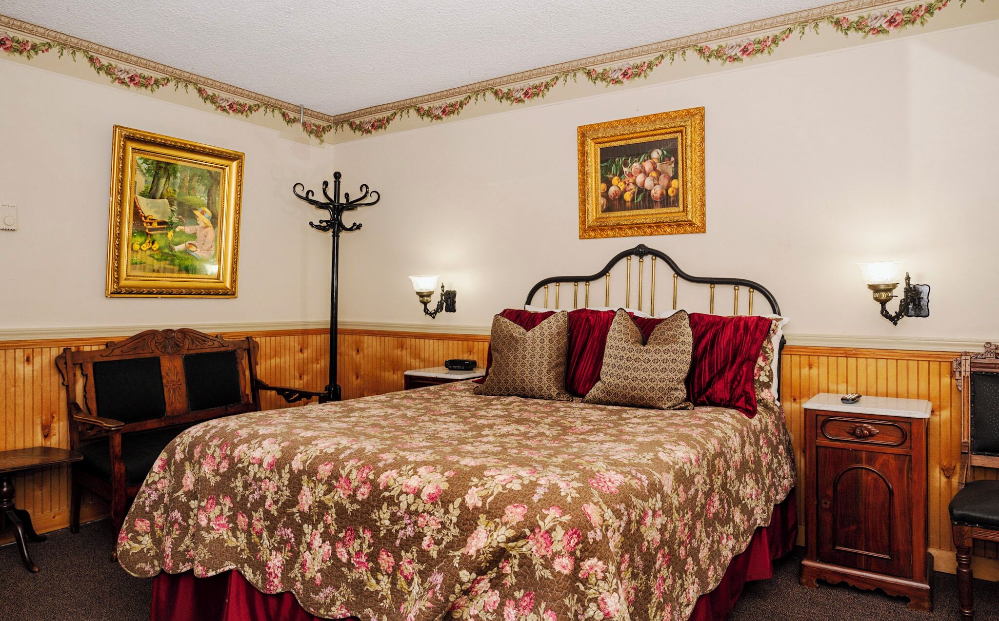 A bedroom with a large bed, two wall-mounted lamps, a wooden bench, and two framed pictures on the wall.