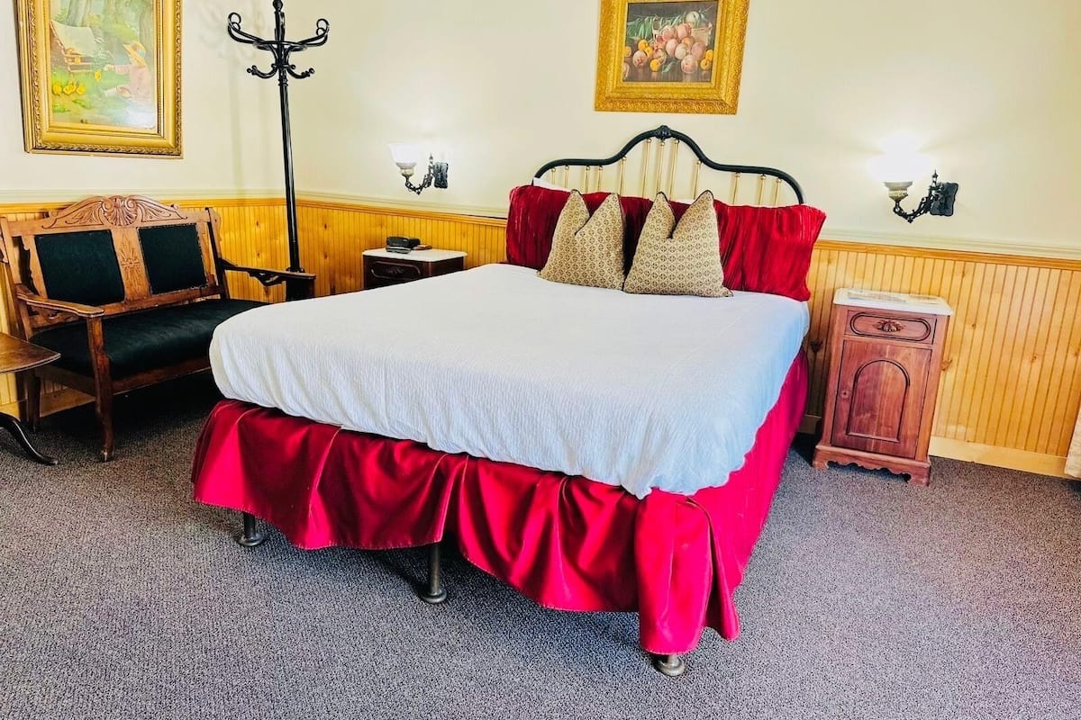A neatly arranged bedroom with a large bed, a wooden bench, a small table, and a cabinet.