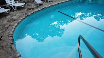 Una piscina con borde de piedra, sillas de descanso y barandilla de metal.