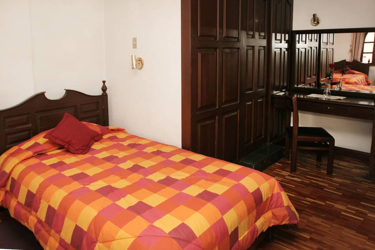 A bedroom with a wooden bed, a desk with a chair, and a mirror.