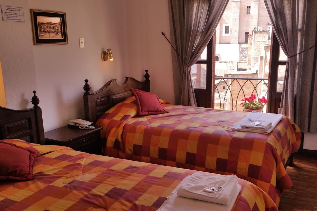 A hotel room with two beds, a nightstand, a telephone, a framed picture on the wall, and a window with curtains.