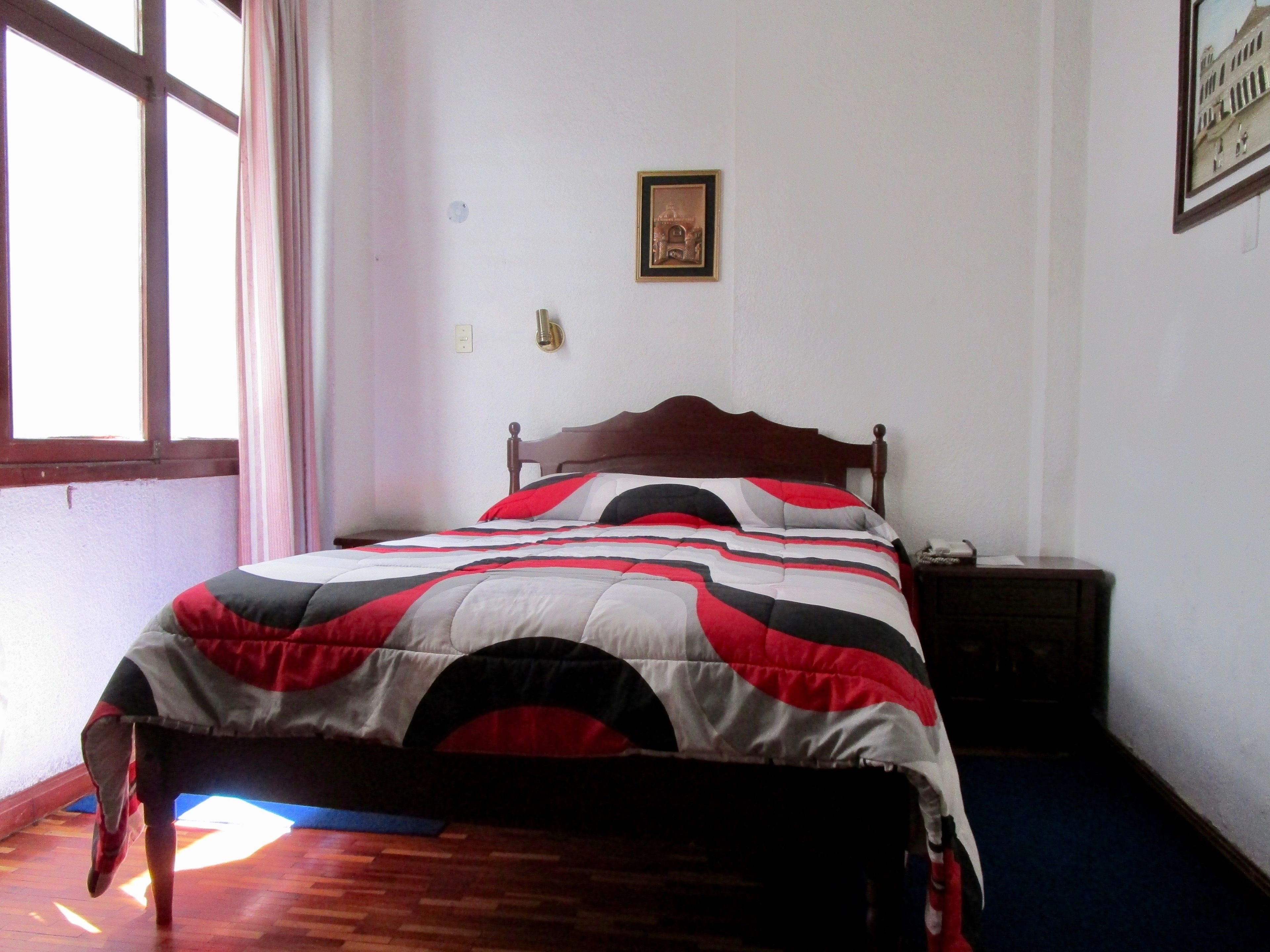 A bedroom with a wooden bed, a nightstand, a framed picture on the wall, and a window with curtains.