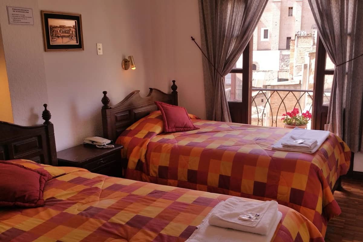 A hotel room with two beds, a nightstand, a telephone, and a window with curtains.